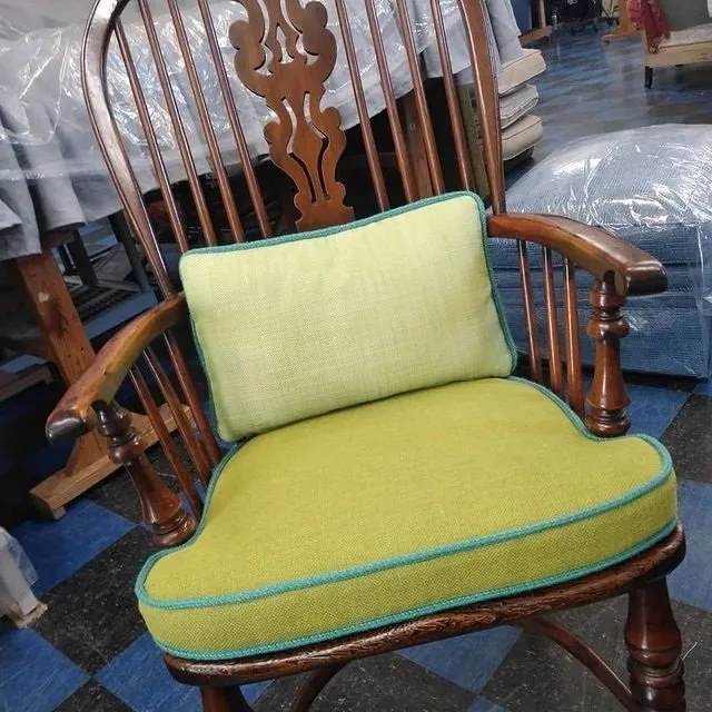 Green upholstered wooden chair with curved arms in a furniture store.