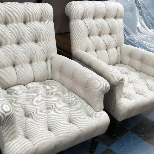 Two white tufted armchairs with armrests on a dark checkered floor.