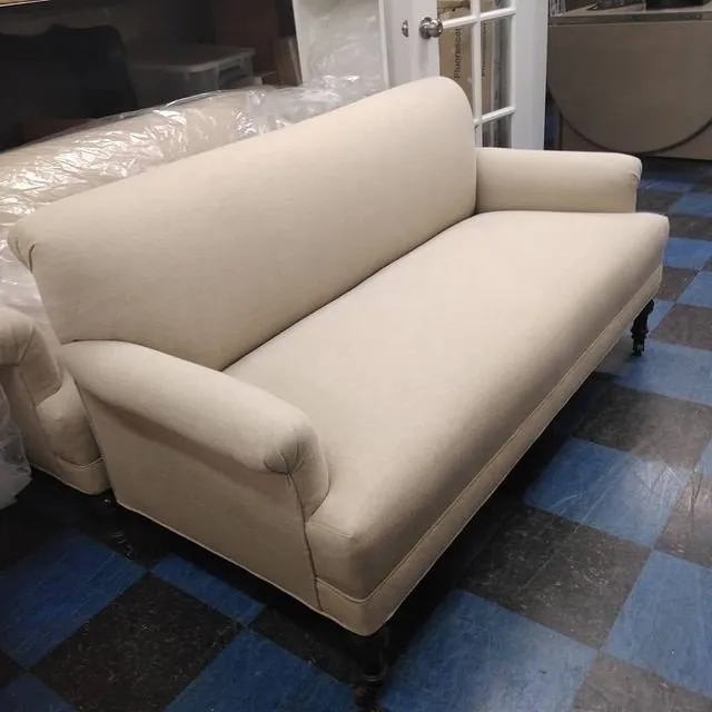 Beige upholstered sofa with rounded arms on a blue and gray checkered floor.