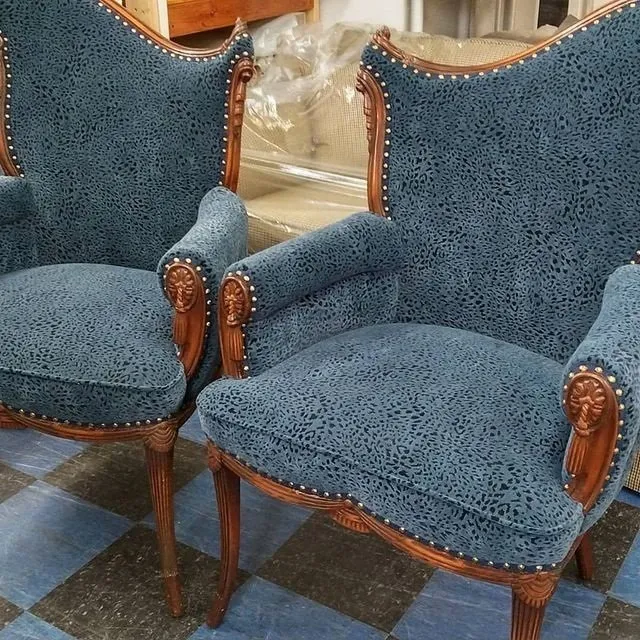 Two blue upholstered armchairs with carved wooden frames in a showroom