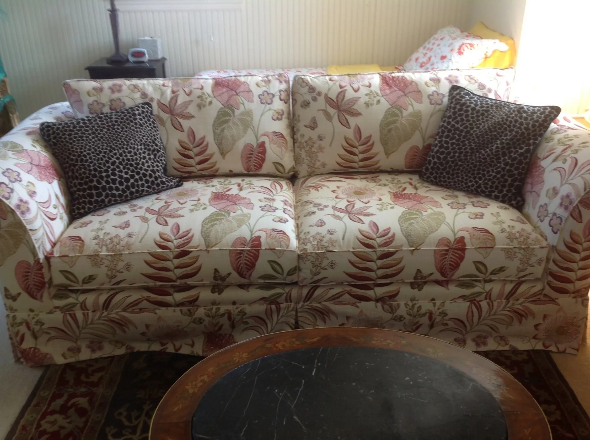 Floral-patterned sofa with black and white pillows in a bright living room, with a round coffee table in front.