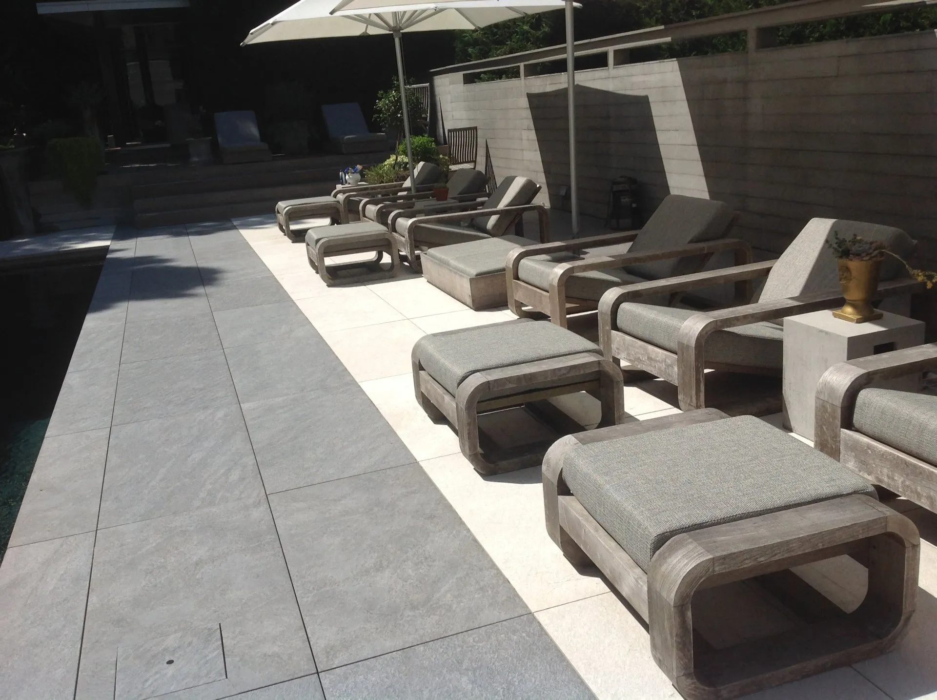 Row of gray lounge chairs and umbrellas on a sunny outdoor patio beside a building