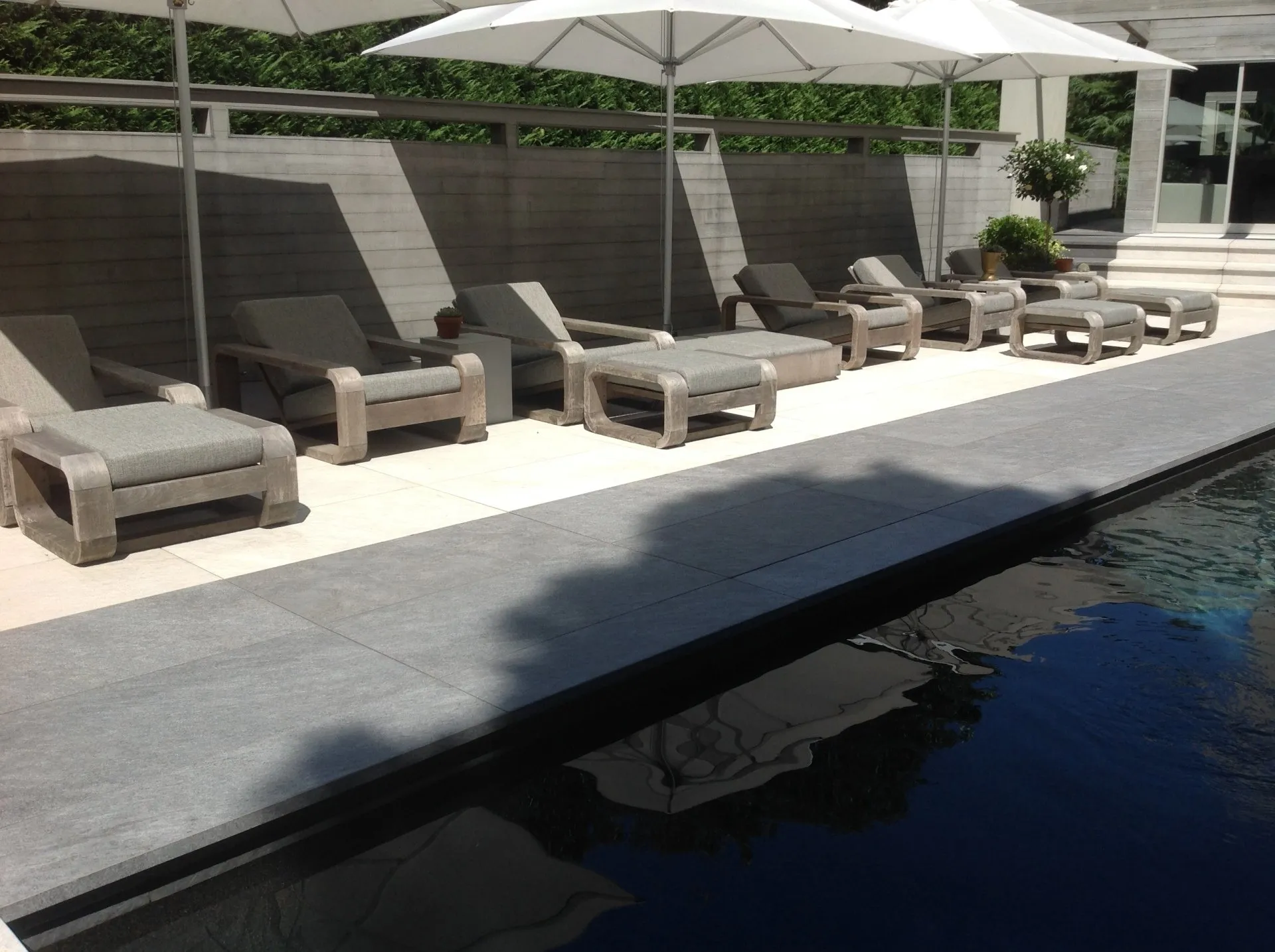 Poolside lounge chairs and white umbrellas beside a modern swimming pool.