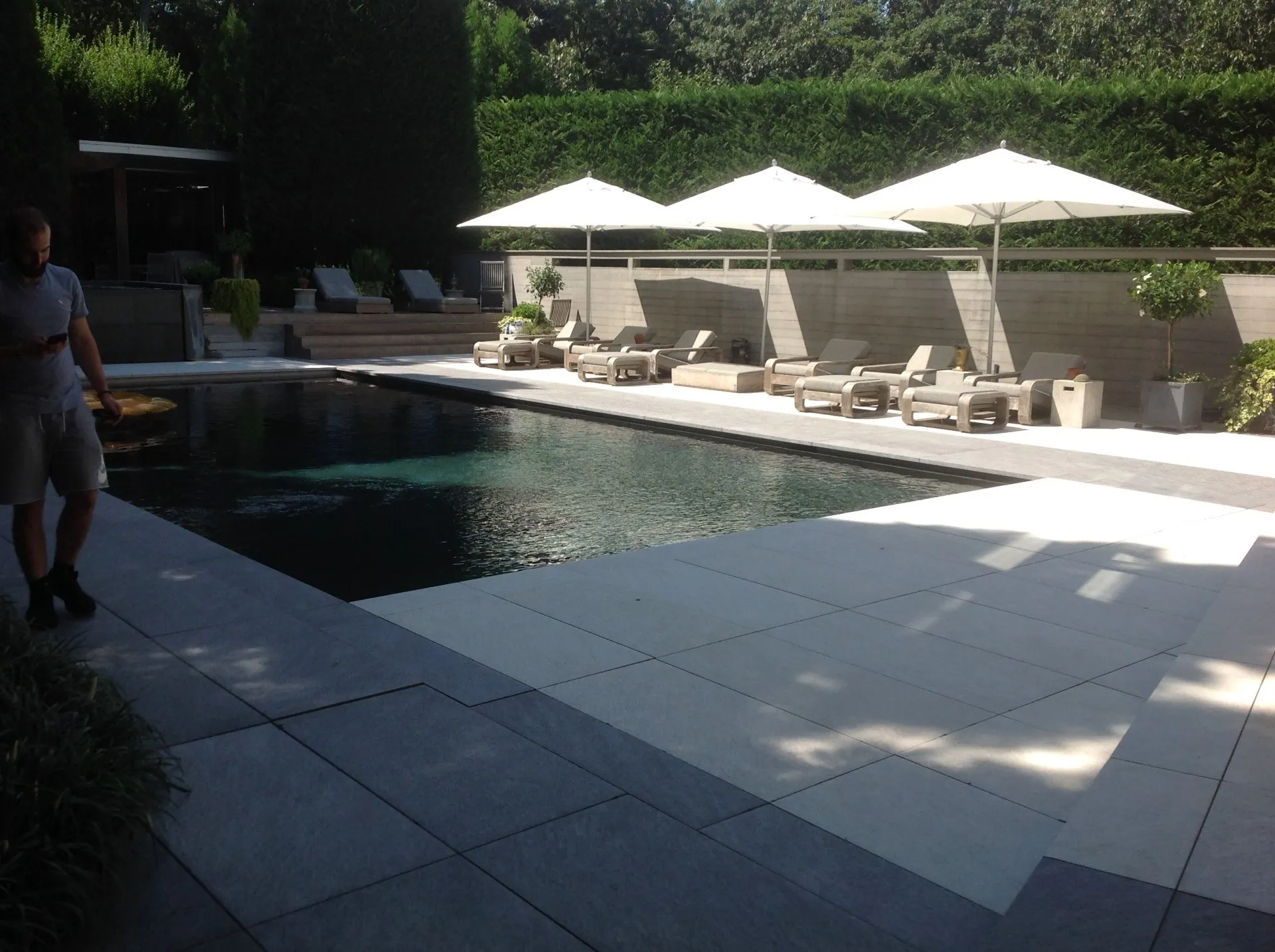 Sunlit hotel pool with white umbrellas and lounge chairs beside a shaded patio