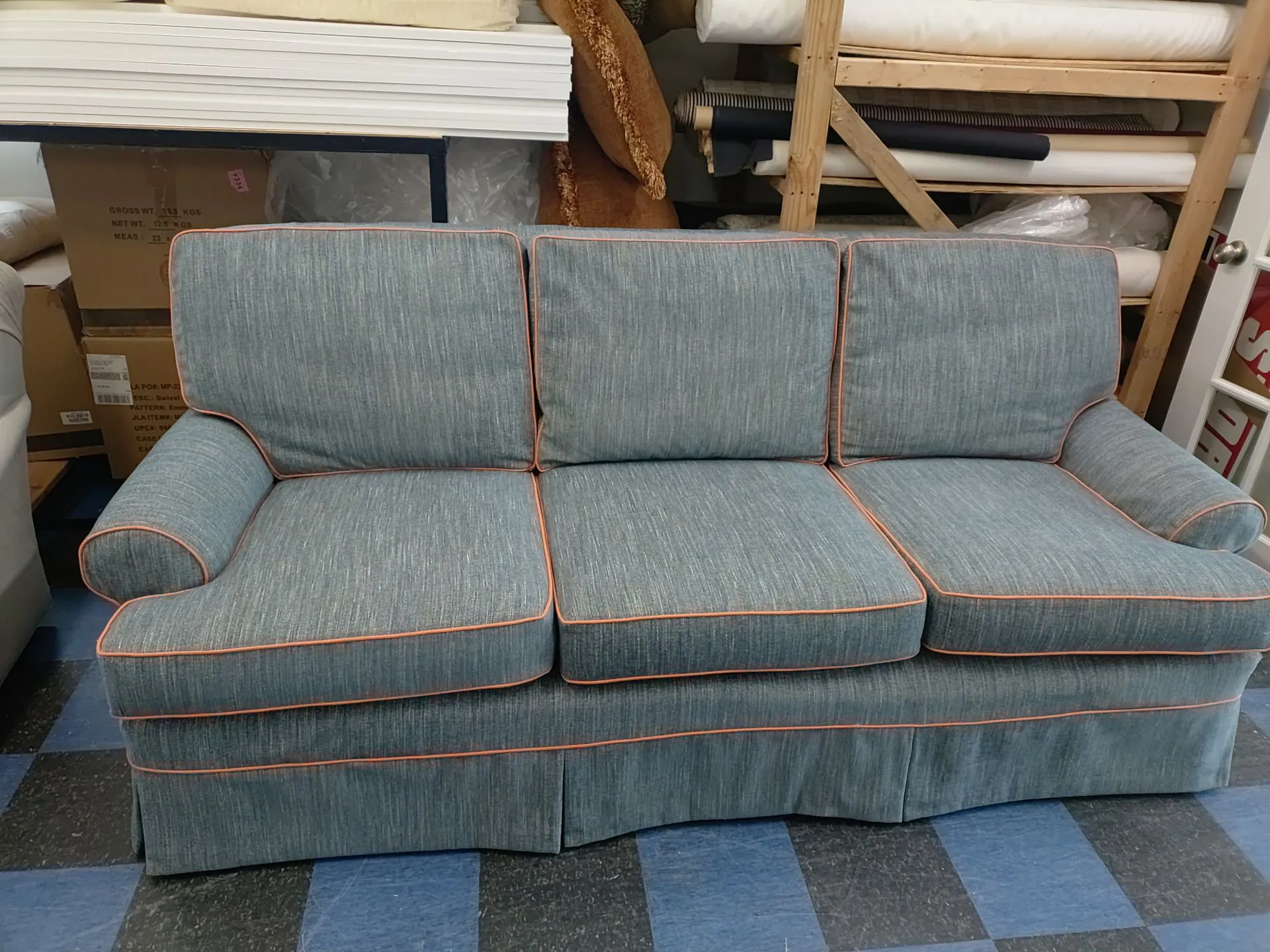 Blue upholstered sofa with orange piping in a storage area