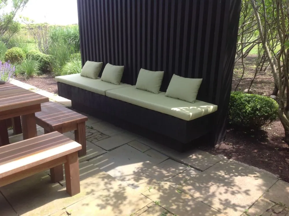 Outdoor lounge bench with green cushions beside a wooden picnic table in a shaded garden area