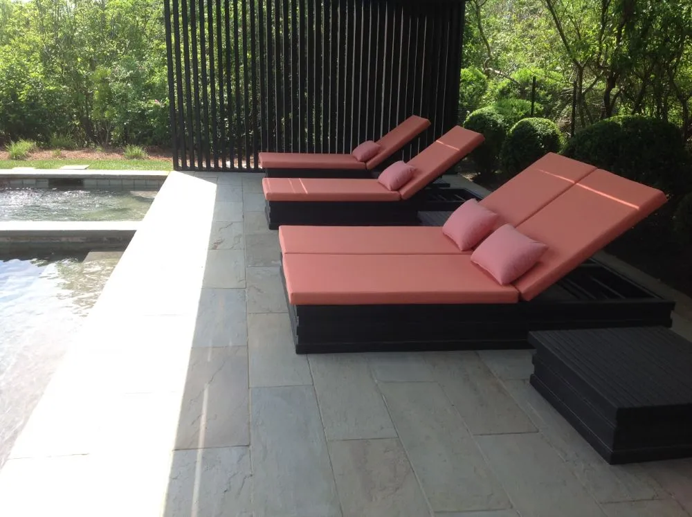 Modern poolside lounge chairs with red cushions beside a swimming pool and greenery