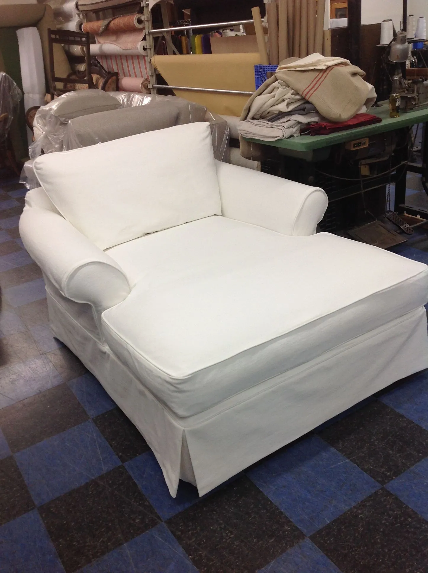 White chaise lounge chair with armrest in a workshop or storage room on a blue checkered floor