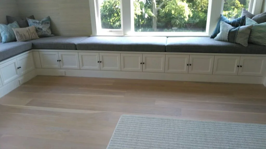 Built-in window seat with white cabinets, gray cushions, and large windows in a bright room