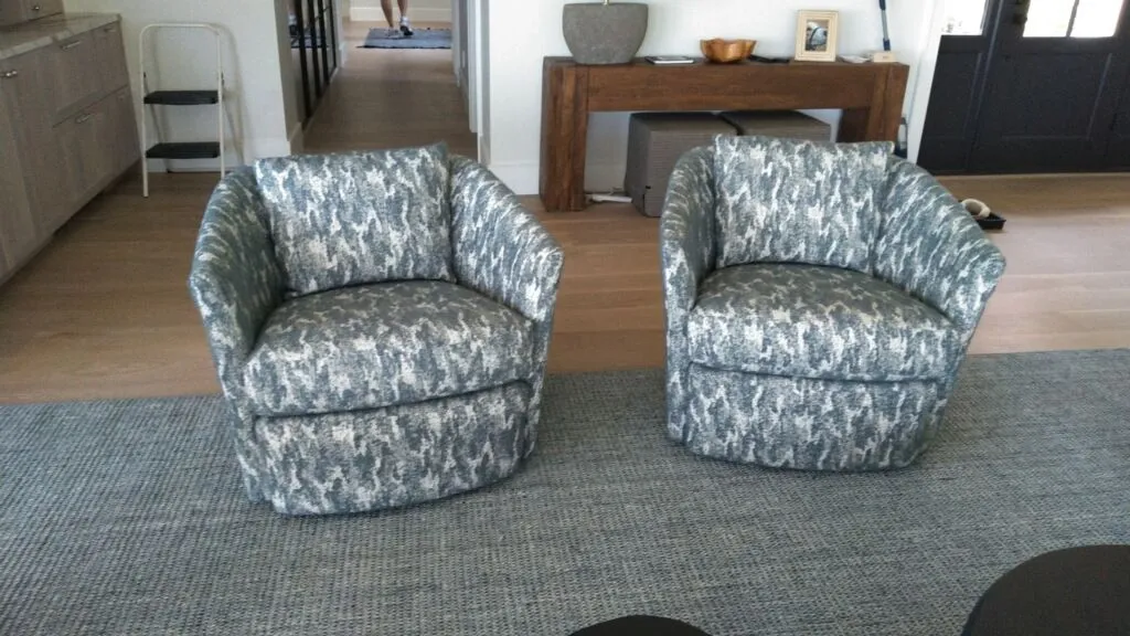 Two patterned armchairs on a rug in a living room, with a console table and hallway in the background