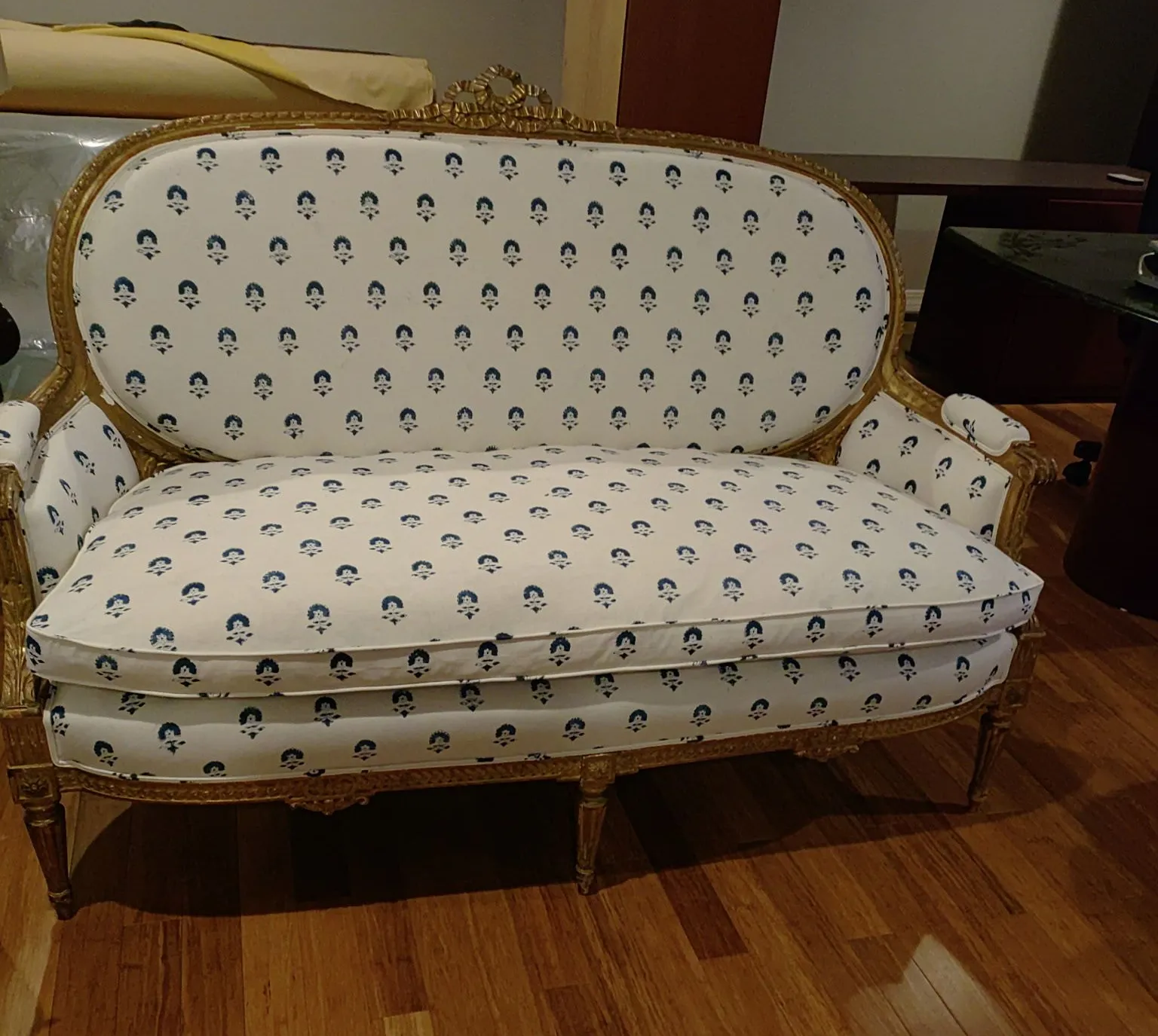 Vintage cream upholstered sofa with blue floral pattern and gold trim in a wooden-floored room