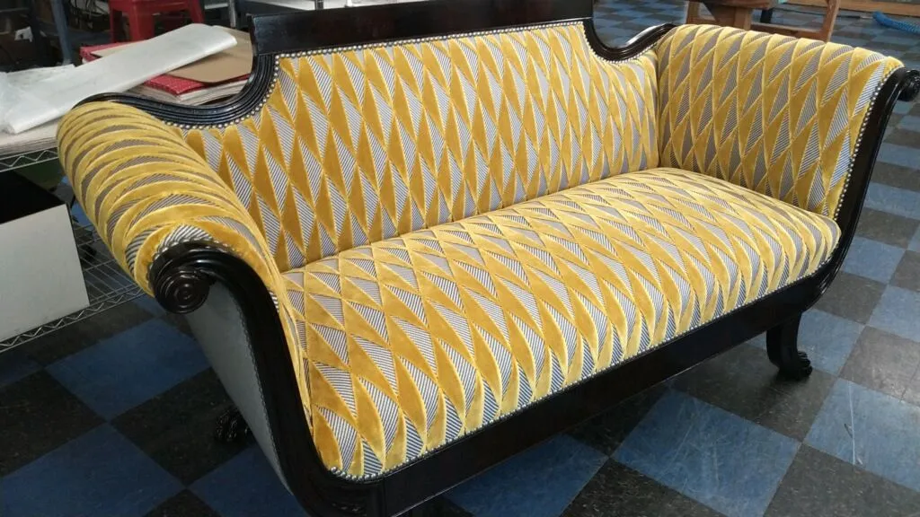 Yellow patterned sofa with black armrests on a blue-and-black checkered floor