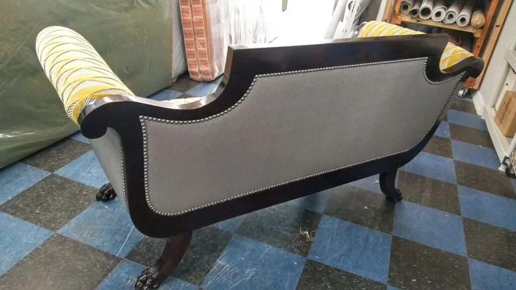 Black upholstered chaise lounge with nailhead trim on a blue-and-black checkered rug