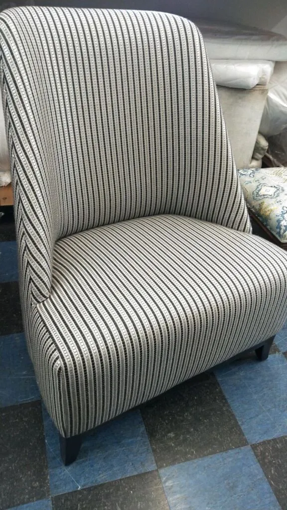 Gray-and-white striped upholstered armchair with dark wooden legs on a blue carpet.