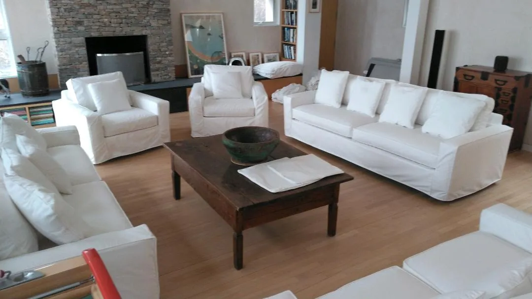 Bright living room with white sofas, wooden coffee table, and stone fireplace.