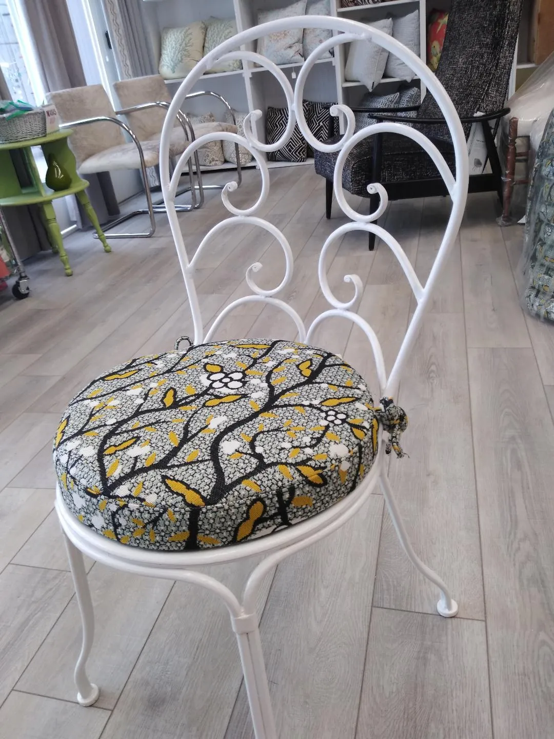 White metal chair with a yellow, gray, and black patterned cushion in a room with light wood flooring