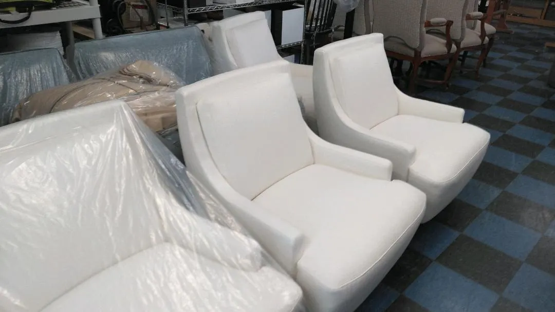 Two white upholstered chairs on a blue-and-black checkered floor in a furniture showroom.