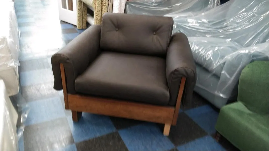 Brown upholstered armchair with wooden base in a furniture showroom, wrapped items nearby