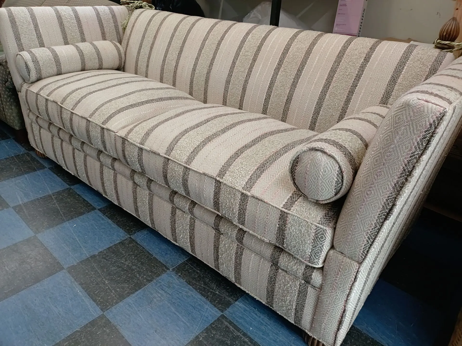 Striped beige upholstered sofa with rolled armrests on a blue checkered floor