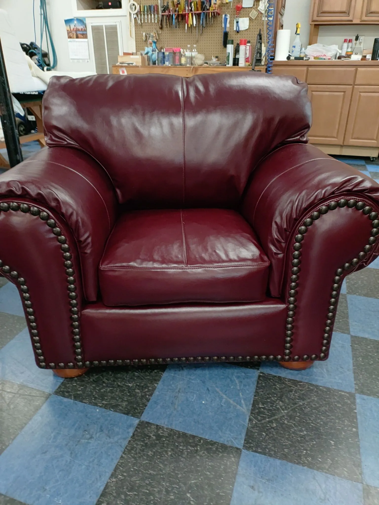 Burgundy leather armchair with nailhead trim on a blue checkered floor in a furniture store