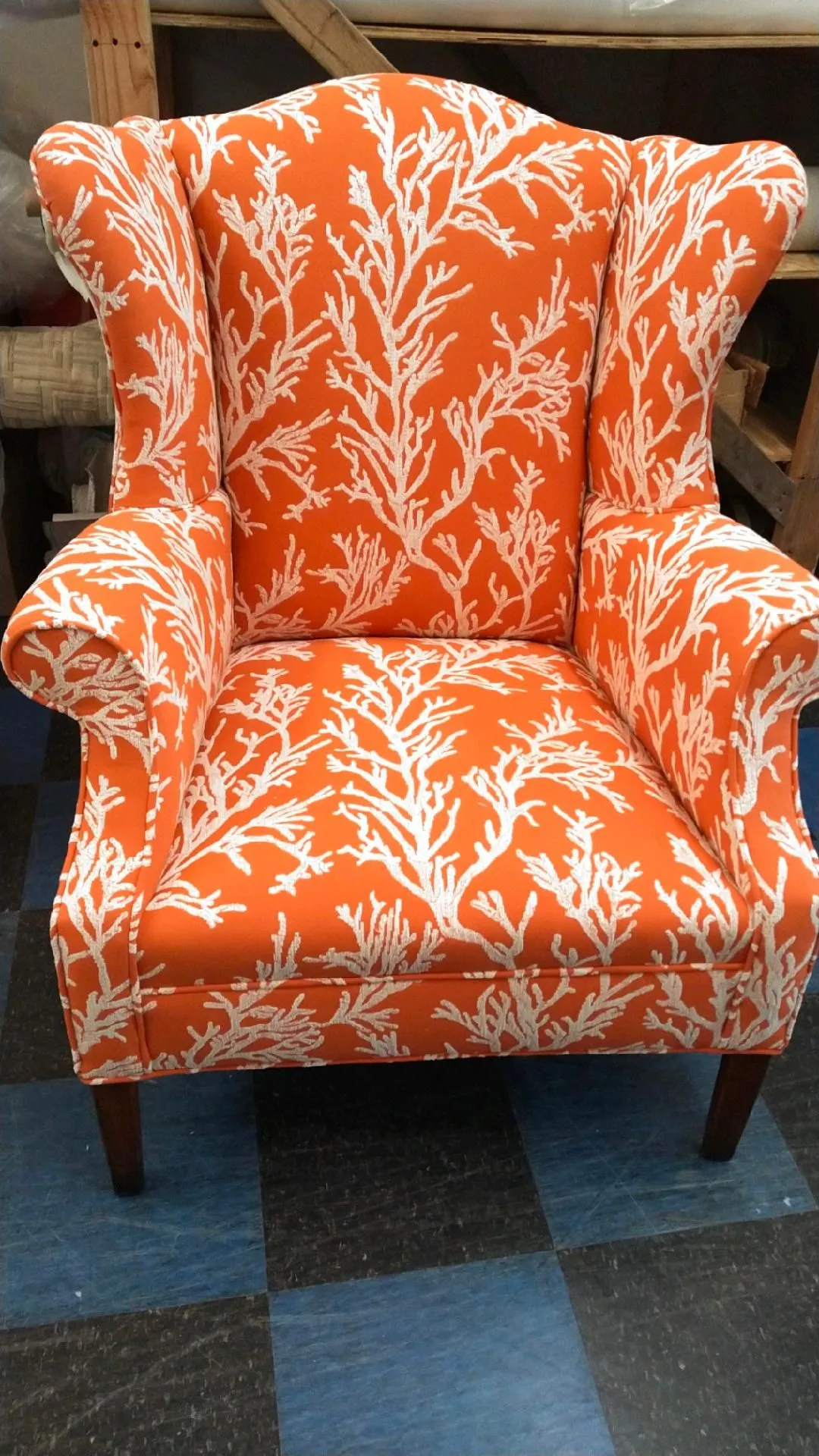Orange floral wingback armchair with wooden legs on a blue carpet.