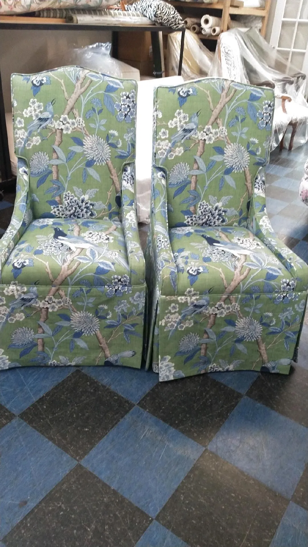 Two green floral-patterned upholstered chairs with white trim on a blue-and-black checkered floor.