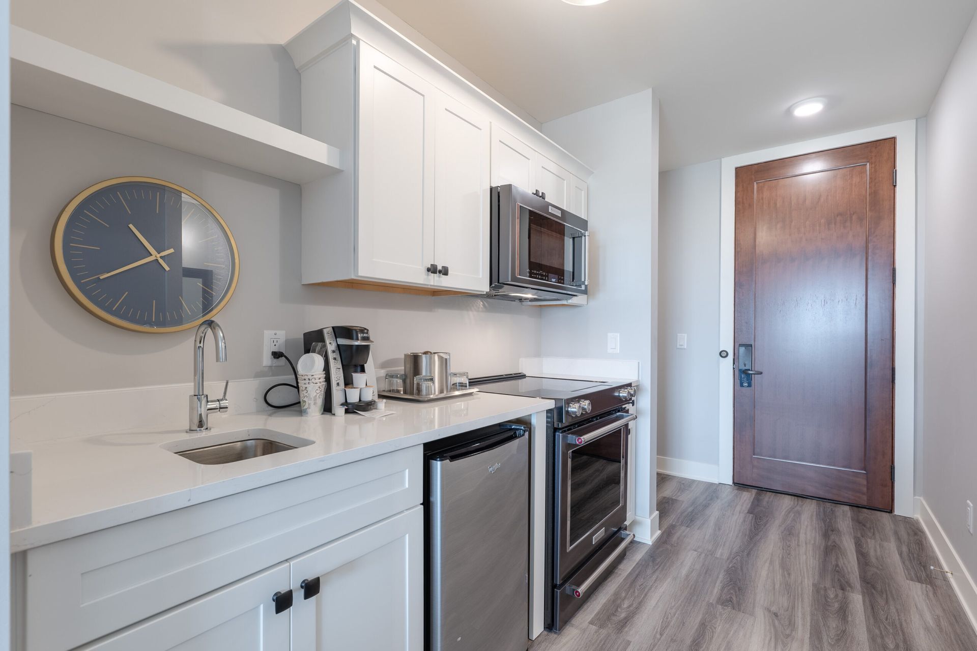 A kitchen with white cabinets , stainless steel appliances , a sink , and a clock on the wall.