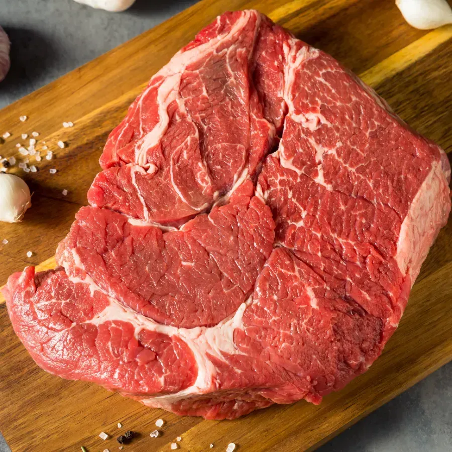 Raw beef roast on a wooden cutting board with garlic and salt.