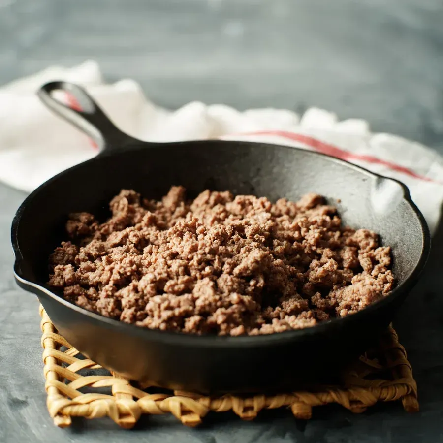 Cooked ground beef in a black cast iron skillet on a woven trivet.