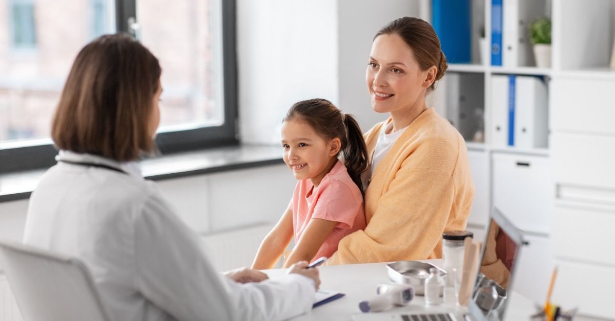 A woman and child smiling while seated across from a person with a clipboard at a desk in a medical
