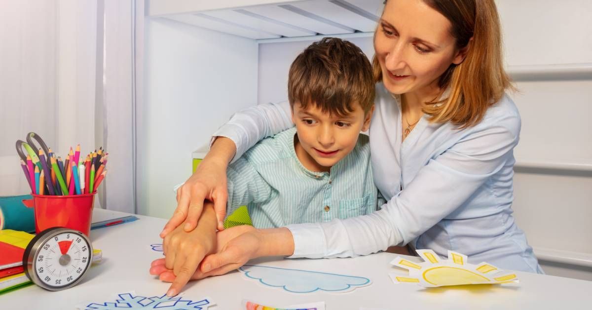 A young boy being assisted to point at a snowflake on a piece of paper by a woman sitting with him.