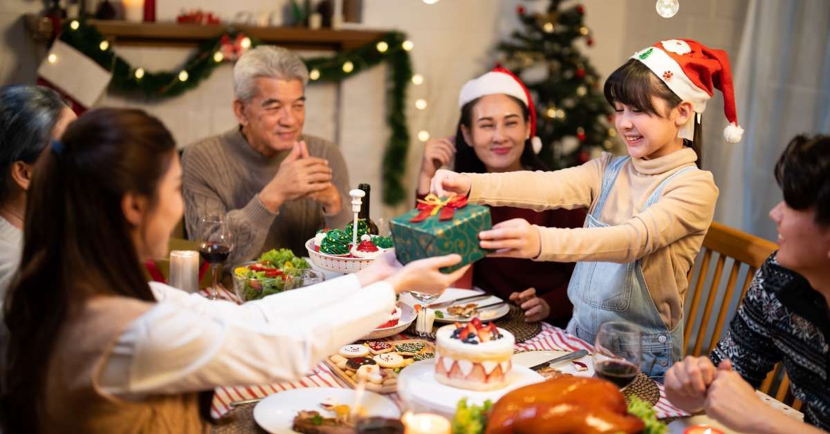 An Asian family joyfully gathers around the Christmas dinner table with gifts.