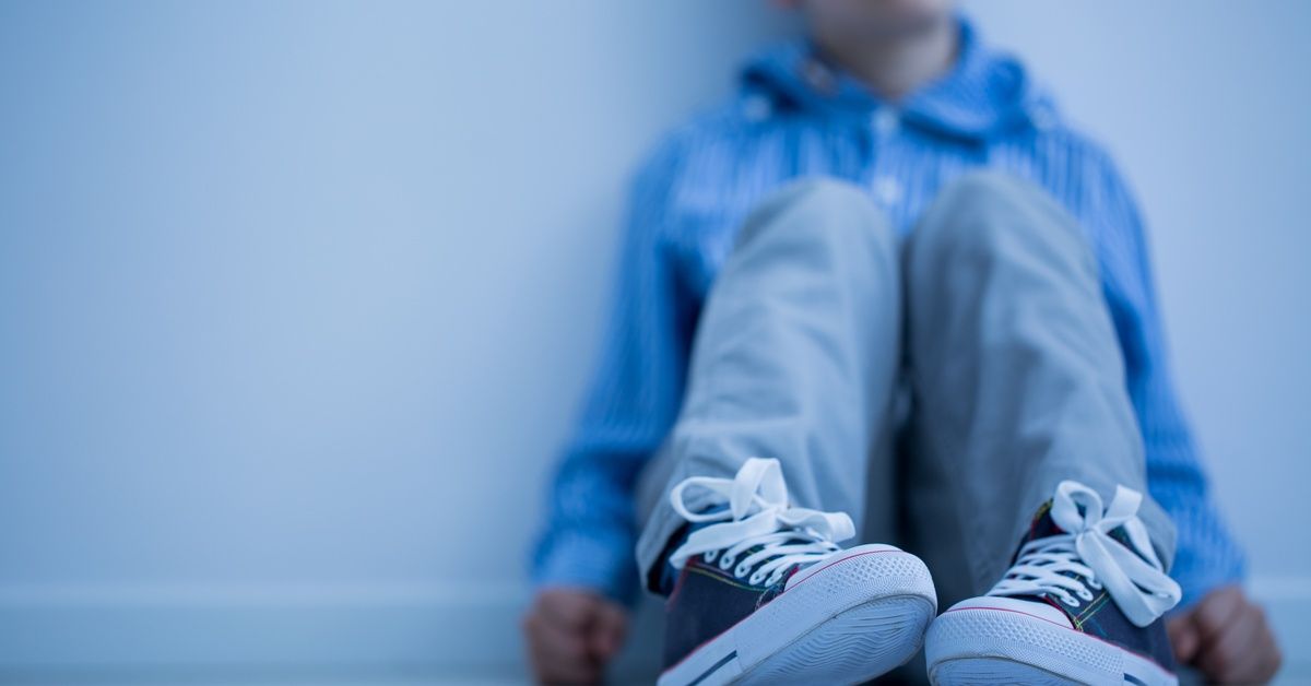 A boy sits against a wall. His dark sneakers with white laces and soles are in sharp focus.