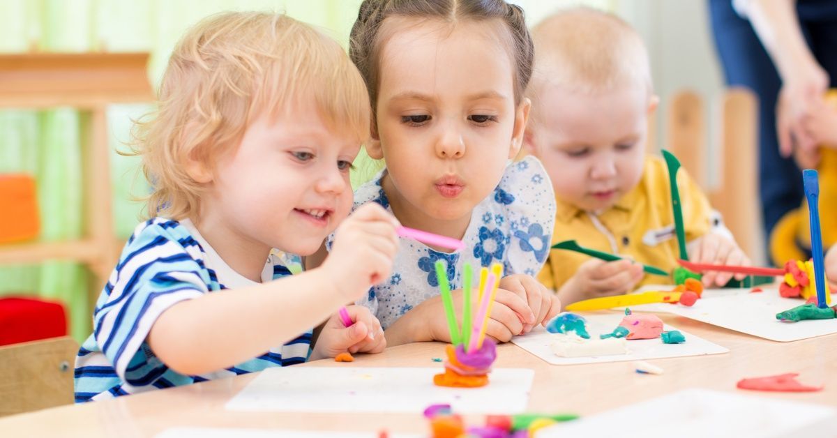 Young children create art with colorful clay and craft sticks at a table during a preschool activity session.