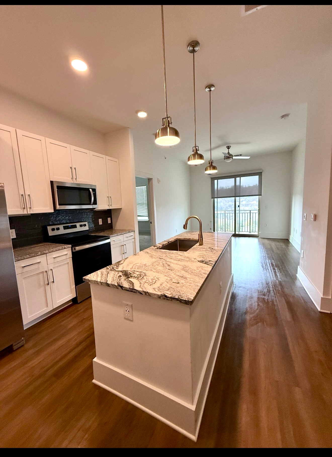 Modern kitchen with white cabinets, granite island, pendant lights, and hardwood floors leading to a bright dining area