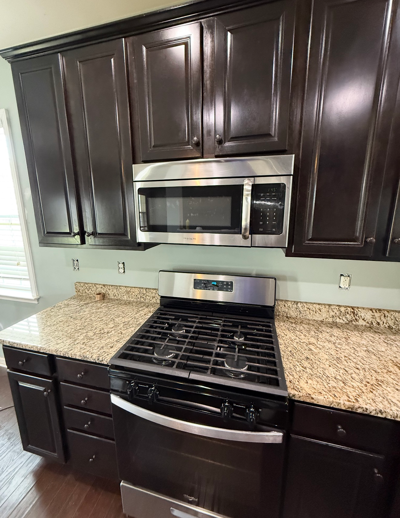 Dark kitchen with stainless stove and microwave, dark wood cabinets, and light granite countertops