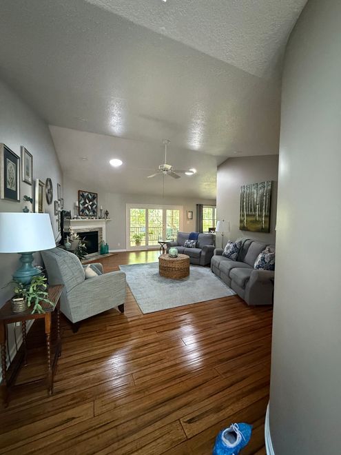 Bright living room with gray sofas, a white chair, wooden floor, and sunlight through large windows.