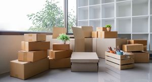 Stacks of moving boxes and packing supplies in a bright, empty room with a window and shelving unit