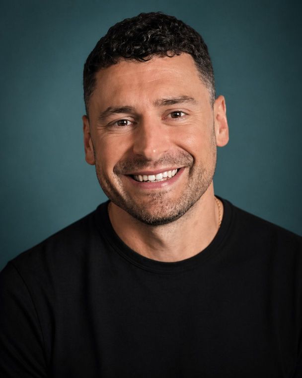 Smiling man in a black shirt against a dark teal studio background.