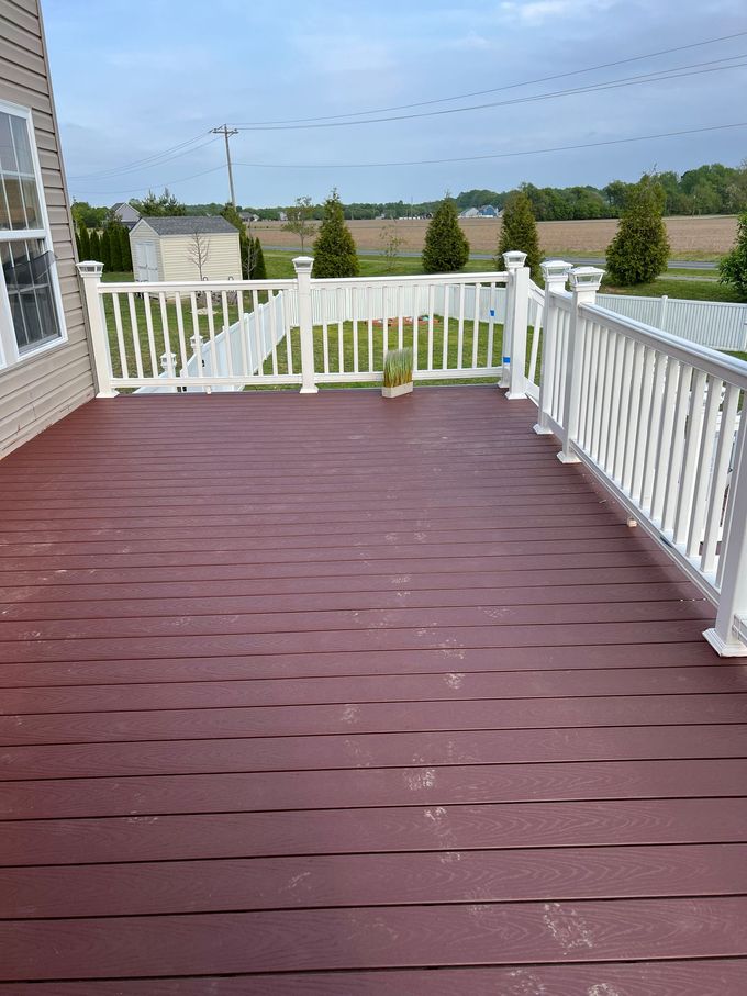 Red wooden deck with white railings overlooking a suburban landscape under cloudy skies