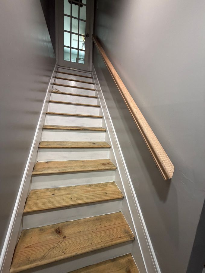 Steep indoor staircase with wooden steps, gray walls, and a handrail leading to a door at the top