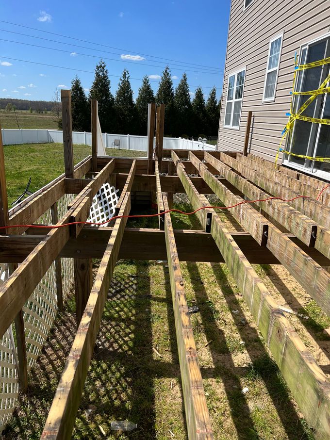 Wooden deck under construction beside a house, with exposed joists and supports in a sunny backyard.