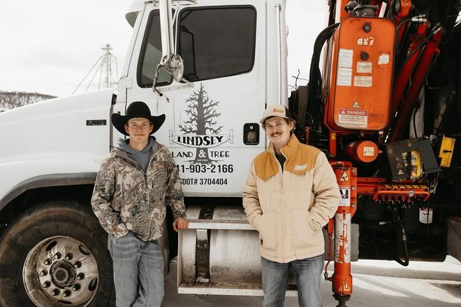 Two workers standing by a white truck with an orange crane attachment in a snowy lot
