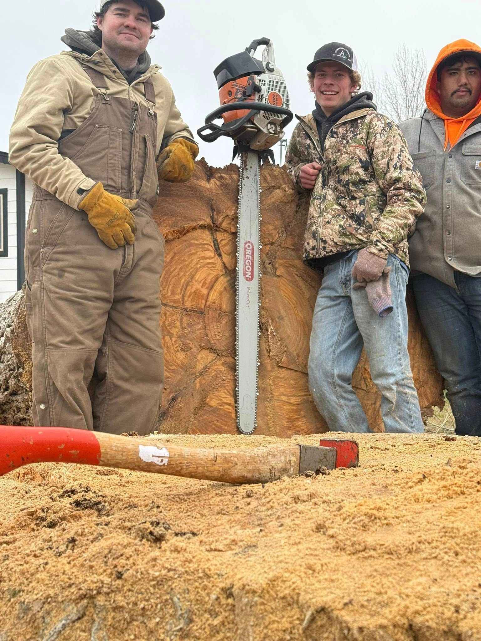 Three workers stand by an auger drilling into a sawdust pile at an outdoor work site.