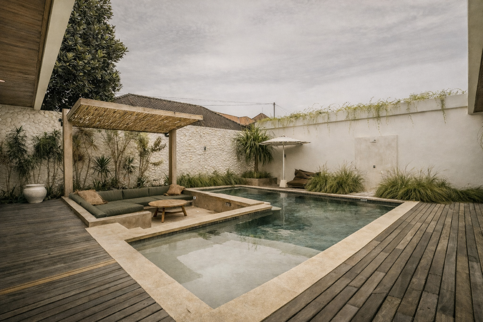 Outdoor pool with a seating area under a wooden pergola, surrounded by a deck and white walls.