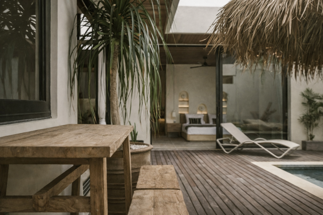 Wooden patio with table and bench, leads to a room with a bed and a pool.