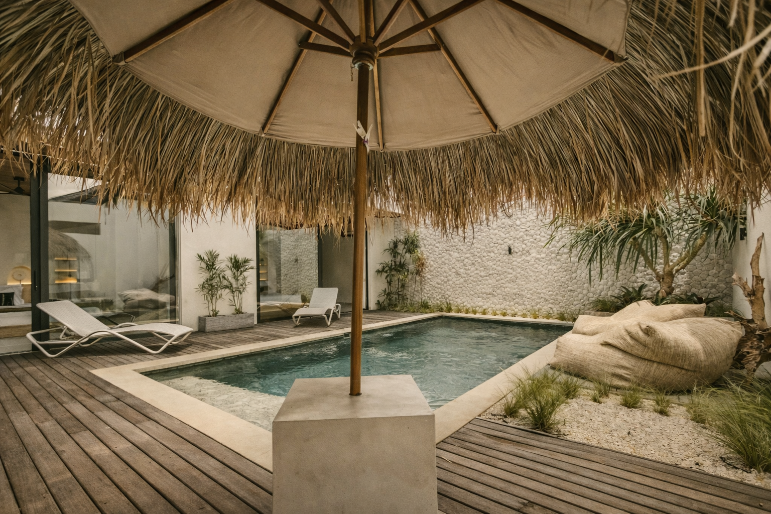 Pool with umbrella and lounge chairs in a courtyard with wooden deck and white walls.