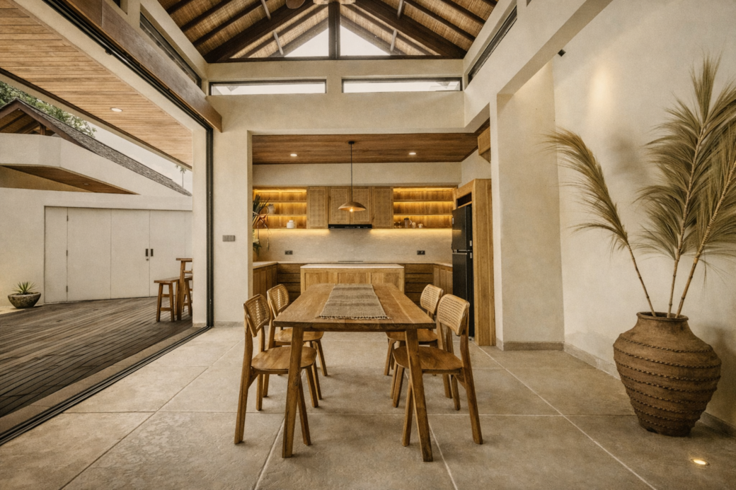Dining area with wooden table and chairs, kitchen in background, large vase with plant.