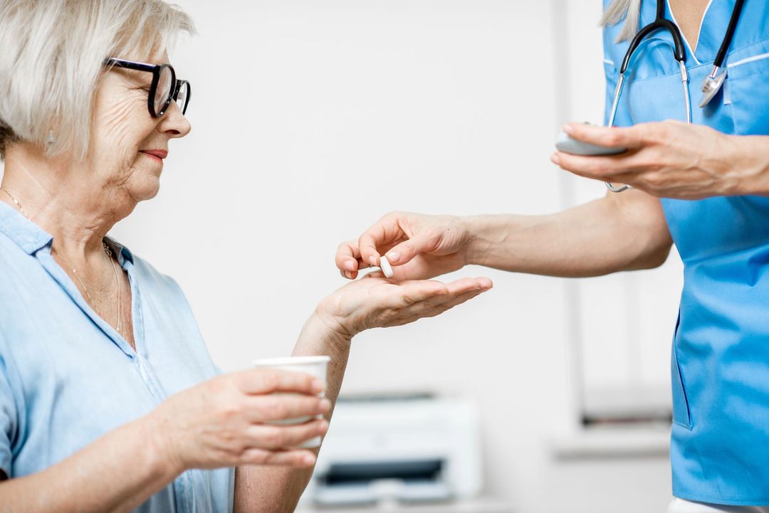 Un operatore sanitario in uniforme blu mette una pillola nella mano di una persona che tiene in mano un misurino per medicinali.