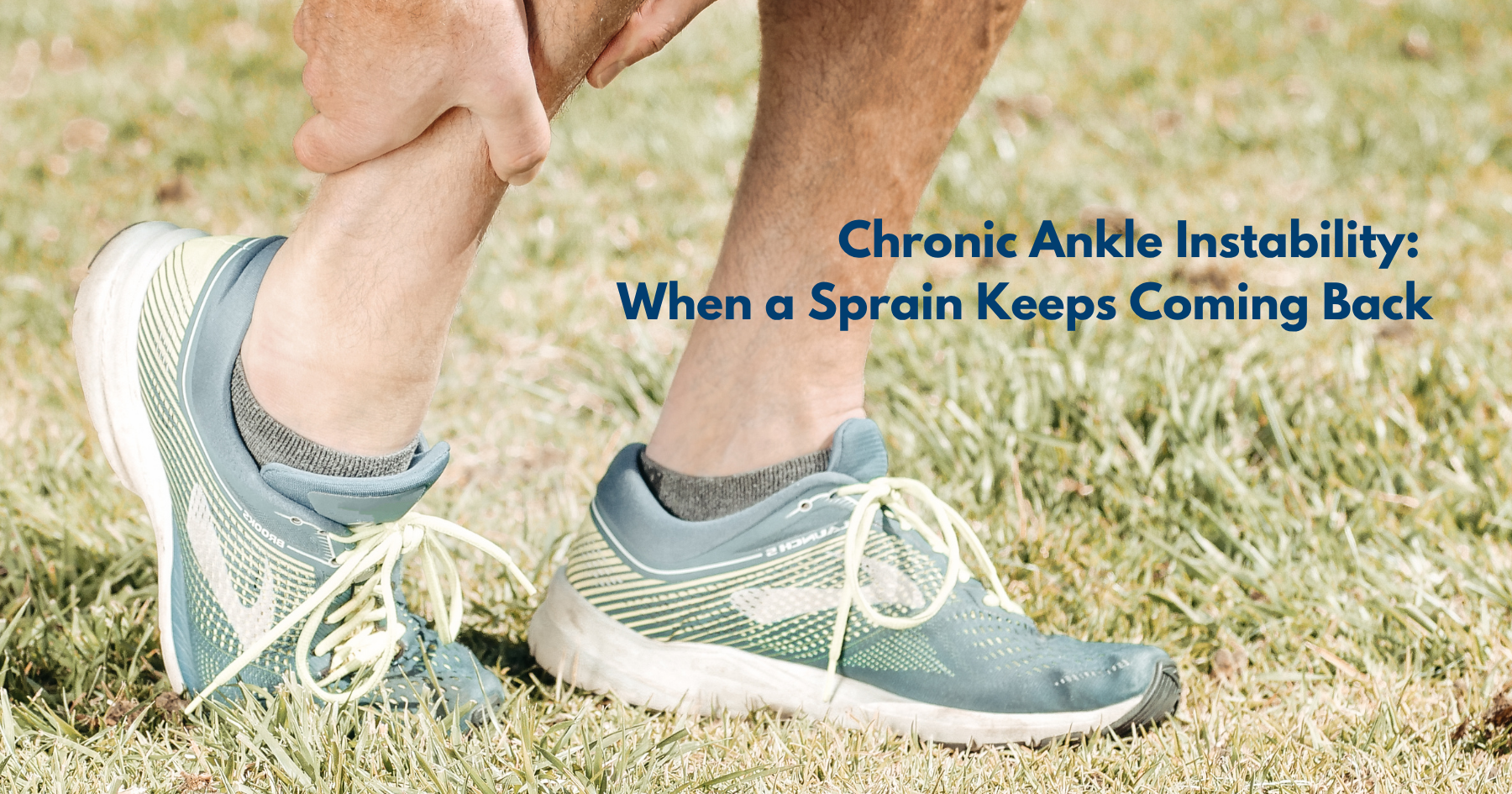 Person in running shoes standing on grass, bending down to hold a sore ankle after rolling it.